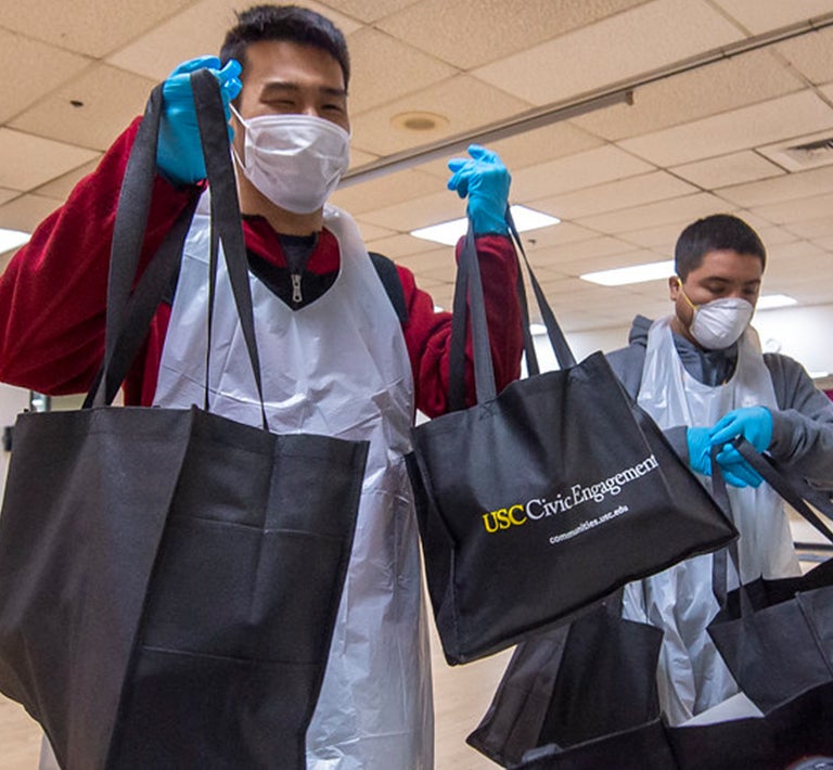 Volunteers in masks handing out supplies in a USC Civic Engagement bag