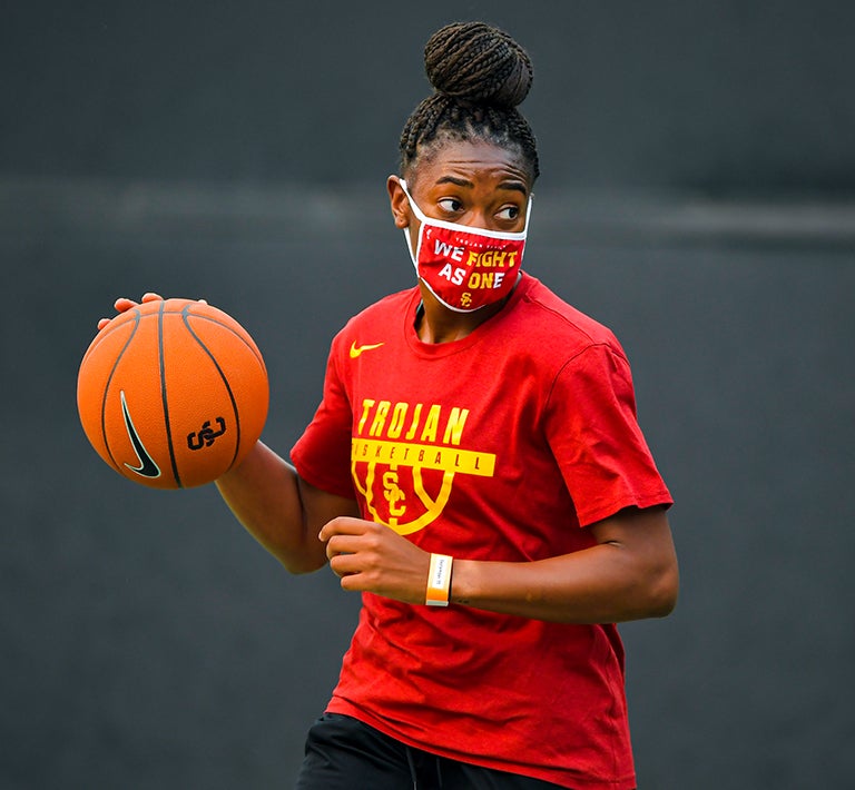 USC women's basketball player wearing a mask and dribbling a ball.