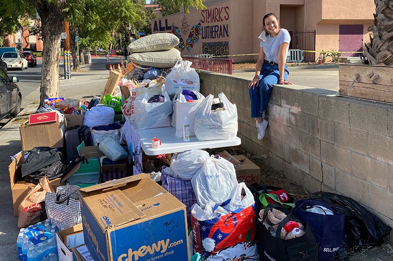 USC student volunteering to help the homeless sites on a wall in front of supplies 