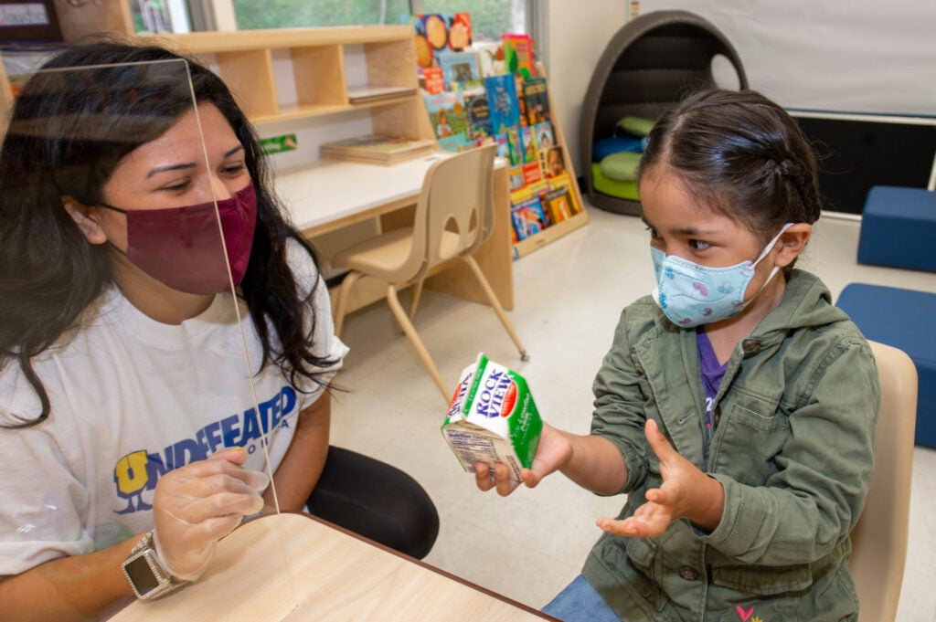 Associate Teacher Jenny Jimenez helps Emily Claudio, 4, with her milk carton on her first day of school.
