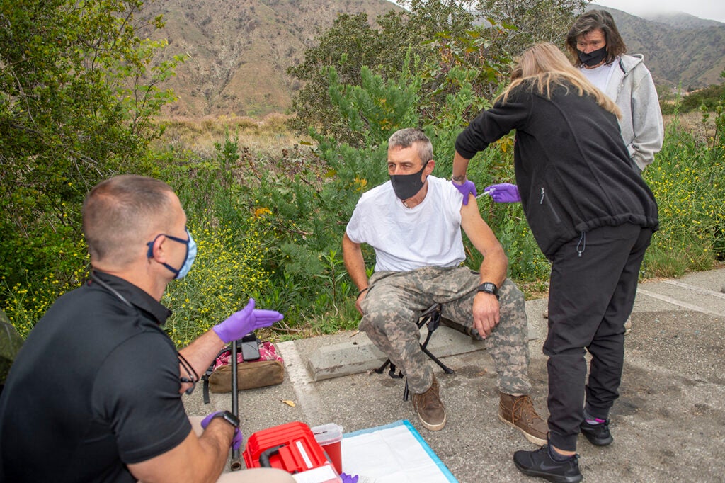 Frank Jauch, far right, watches Sandra Valencia, LVN, center right, administer a COVID-19 vaccination to Kevin Mowrey, center left, while Brett Feldman, PA, left, talks with him. 