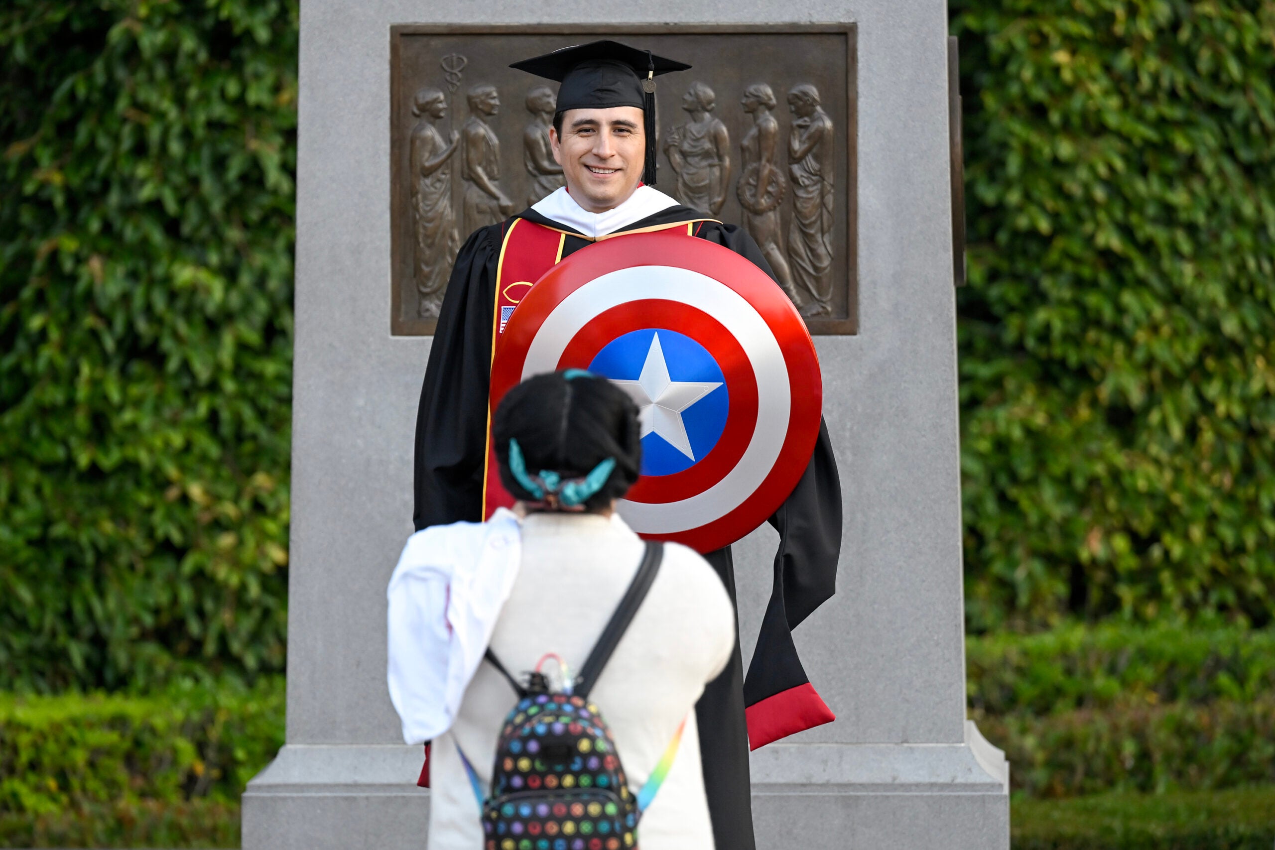 Graduate and Avengers fan Charles Hughes has his girlfriend Joanna Teeson take a picture of him with his Captain America shield during the 140th commencement ceremony at the University of Southern California, May 12, 2023. (Photo/Gus Ruelas)