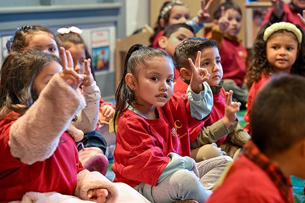 Children sitting hold up the two-finger USC "fight on" salute while celebrating the opening of new facilities that include a USC-run preschool and housing for homeless veterans and their families.