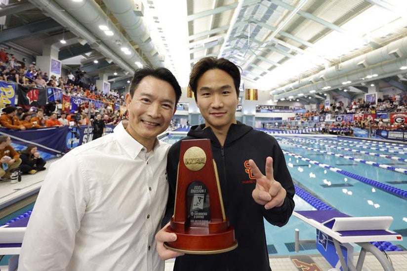 A team member holding up a trophy in front of a swimming pool.