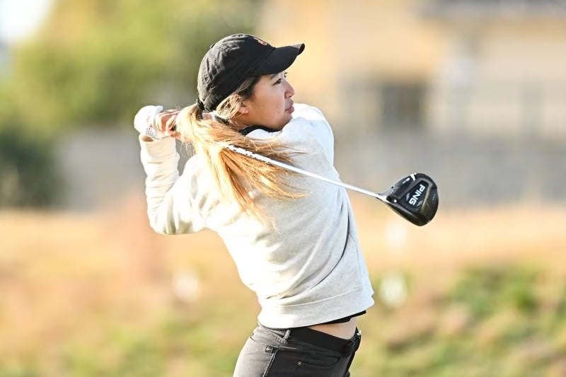 A member of the woman's golf team hitting a golf ball on the course.
